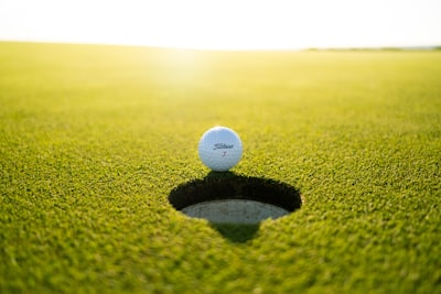 Symbolbild: Golfball am Lochrand im Gegenlicht