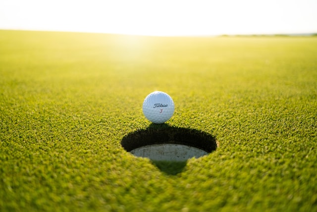 Symbolbild: Golfball am Lochrand im Gegenlicht