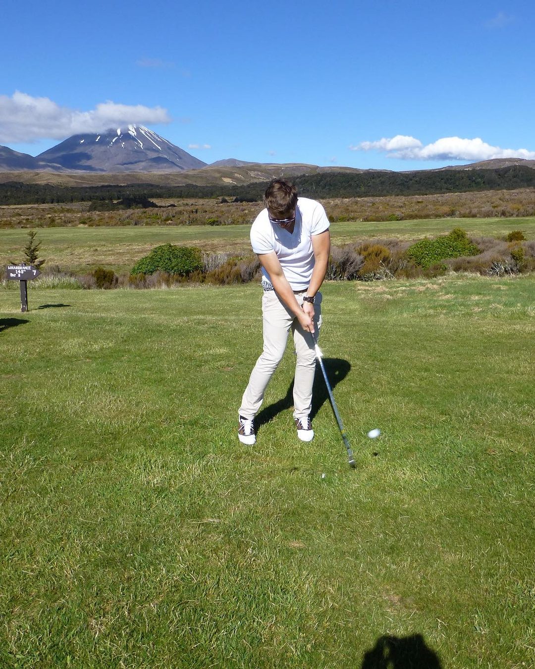 Sebastian Scholz beim Schlag auf einem Golfplatz in Neuseeland, im Hintergrund ein schneebedeckter Vulkan