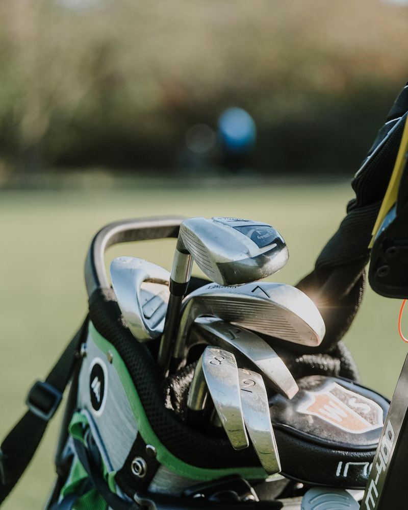 Eisen im Golfbag auf dem Trolley, im Hintergrund ein Fairway